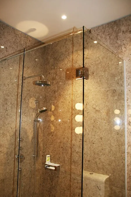 Über Eck gebaute Duschkabine aus Glas mit Natursteinwand