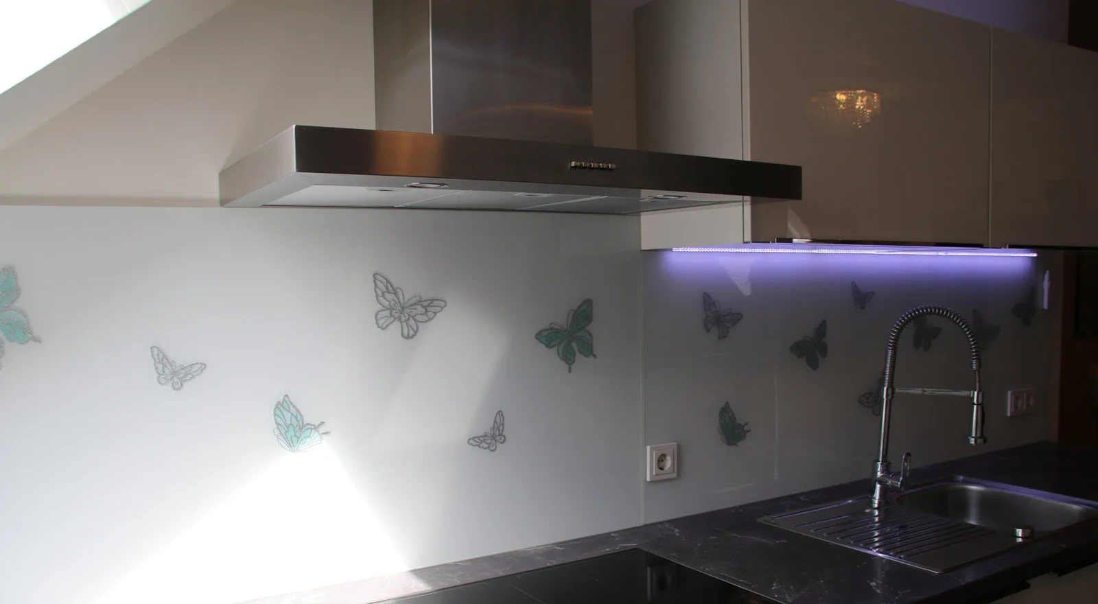 Weiße Küchenrückwand aus Glas mit Schmetterlingsmotiv unter einer Dunstabzugshaube