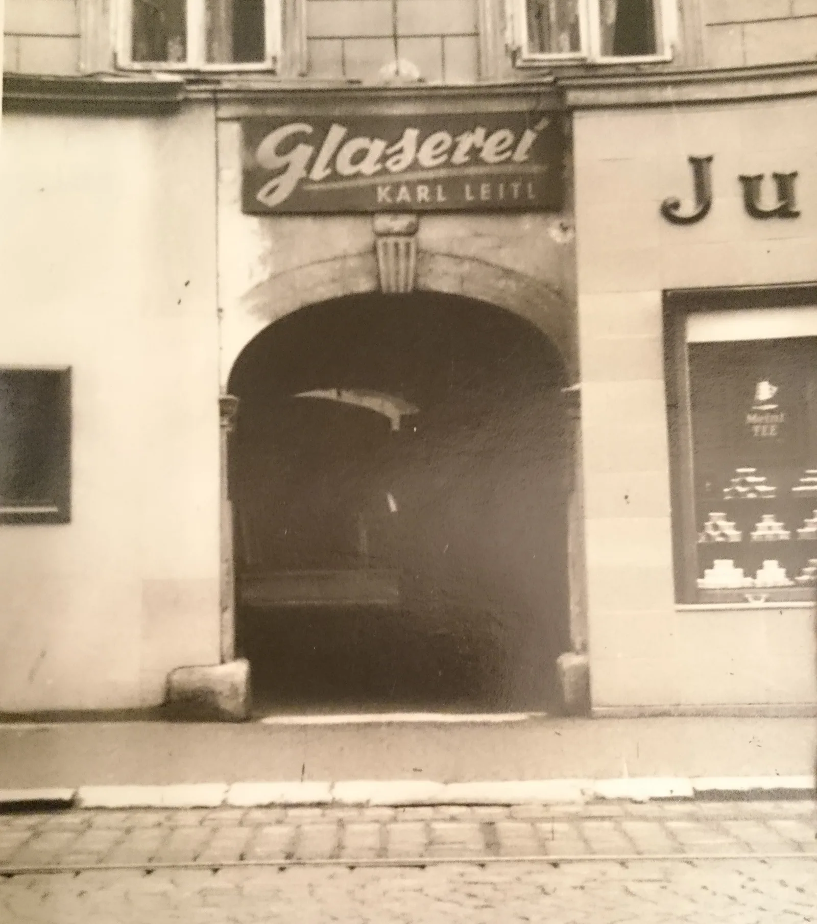 Historische Schwarzweißaufnahme des ersten Geschäfts mit dem Schriftzug Glaserei Karl Leitl über dem Torbogen